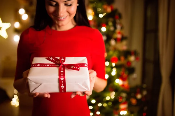 Young woman in front of Christmas tree giving present — Stock Photo, Image