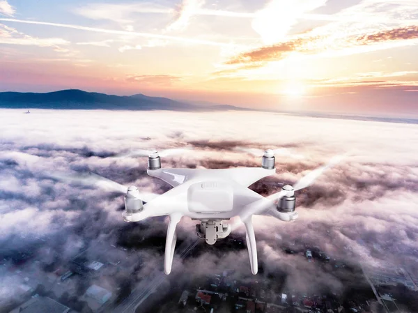 Hovering drone taking pictures of town covered by mist, sunrise
