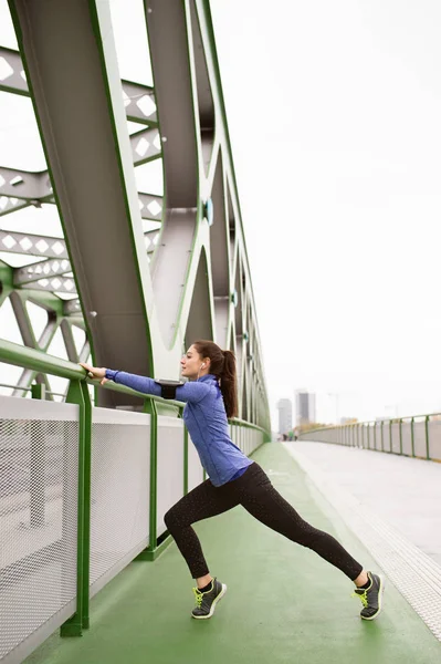 Giovane corridore in città che si estende sul ponte in acciaio verde — Foto Stock