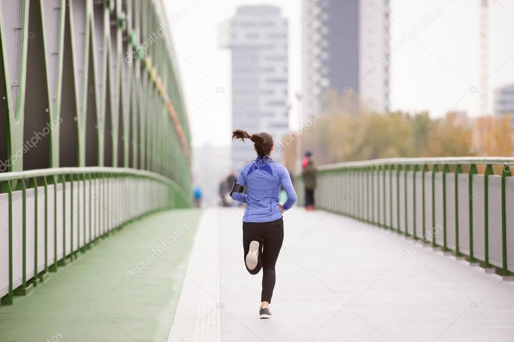 Young woman in the city running on green steel bridge