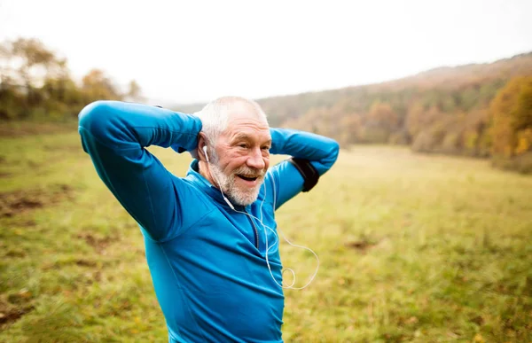 Senior löpare med armband gör stretching. Höstens natur. — Stockfoto