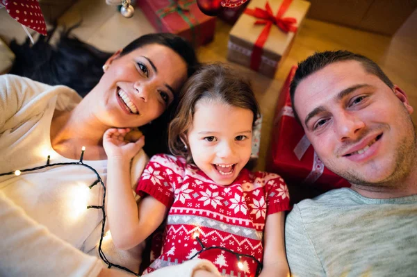 Junge Familie liegt unter Weihnachtsbaum zwischen Geschenken, — Stockfoto