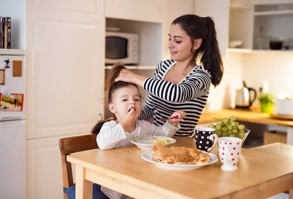 Meisje eten ontbijt, moeder doet haar haren — Stockfoto