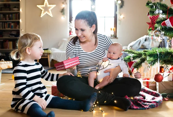 Mother giving daughter Christmas present, holding her son. — Stock Photo, Image