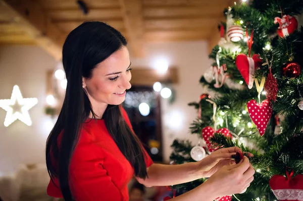 Young woman in front of Christmas tree decorating it — Stock Photo, Image