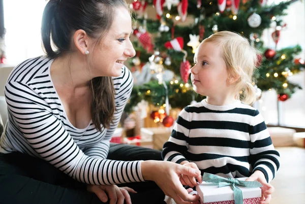 Mãe dando presente filha, árvore de Natal atrás deles . — Fotografia de Stock