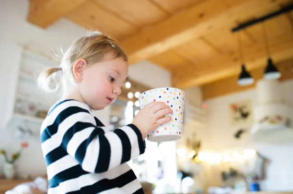 Cute little girl in striped dress sitting on kitchen table, hold — Stock Photo, Image