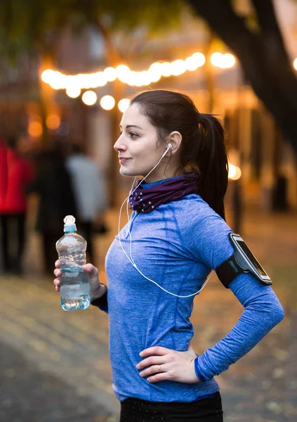 Junger Läufer rastet aus, trinkt Wasser in beleuchteter nächtlicher Stadt. — Stockfoto