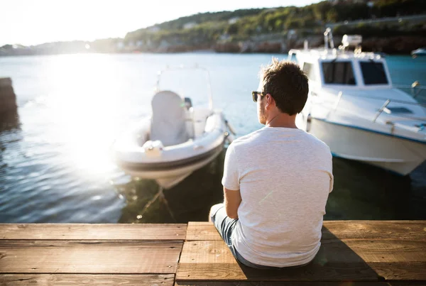 木製の桟橋の上に座って、海辺での時間を楽しむ男. — ストック写真