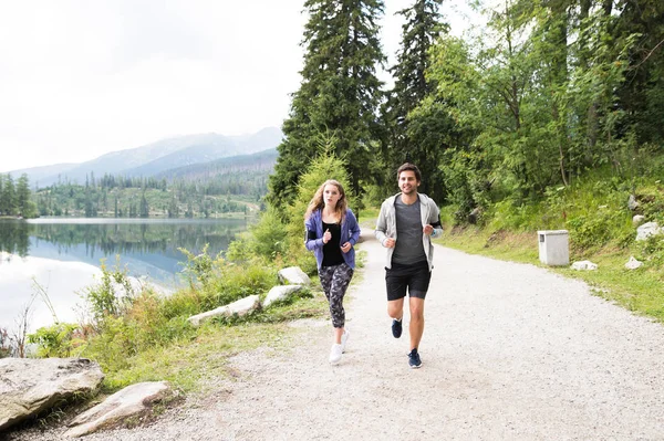 Hermosa pareja joven corriendo en el lago en la naturaleza verde . — Foto de Stock