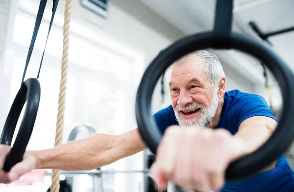 Hombre mayor en el gimnasio haciendo ejercicio en anillos gimnásticos — Foto de Stock