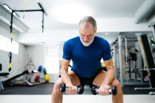 Homme âgé dans la salle de gym travaillant avec des poids, accroupi . — Photo