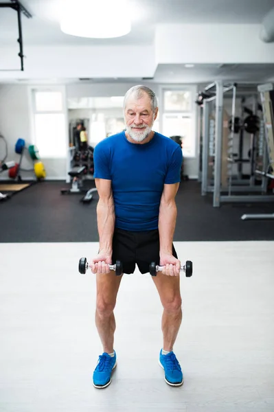 Hombre mayor en el gimnasio haciendo ejercicio con pesas . — Foto de Stock