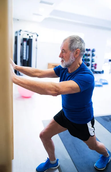 Uomo anziano in palestra che si allena, allungando le gambe — Foto Stock