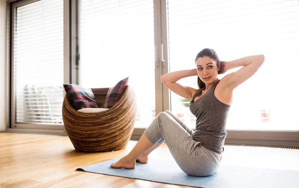 Ung kvinna träna hemma, gör crunches. — Stockfoto