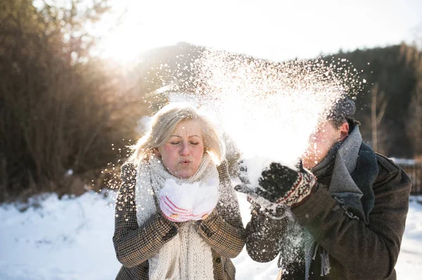 Casal sênior bonito soprando neve na natureza ensolarada inverno — Fotografia de Stock