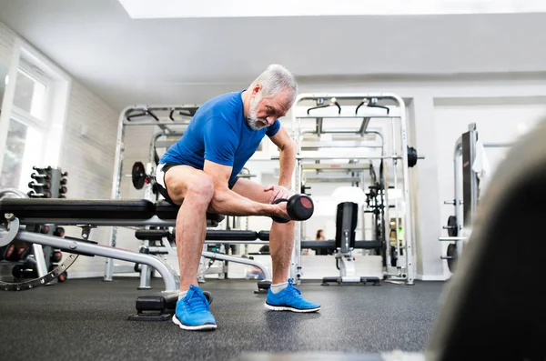 Hombre mayor en el gimnasio haciendo ejercicio con pesas . — Foto de Stock