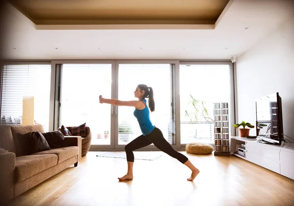 Jovem mulher se exercitando em casa, esticando pernas e braços . — Fotografia de Stock