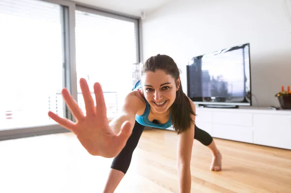 Ung kvinna utöva hemma, stretching ben och armar. — Stockfoto