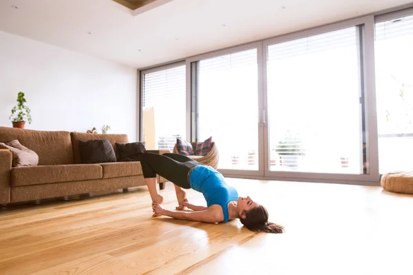 Ung kvinna utöva hemma, stretching, gör bron pose. — Stockfoto