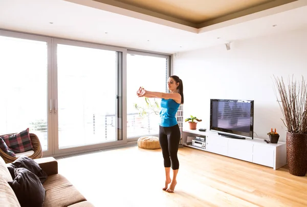 Jovem se exercitando em casa, esticando os braços . — Fotografia de Stock