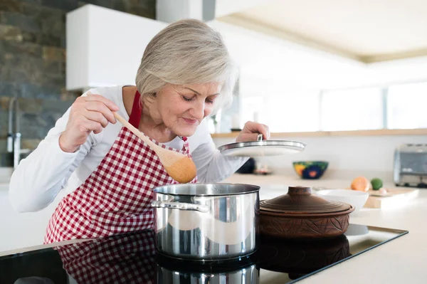 Senior woman in the kitchen cooking, mixing food in a pot. — Stock Photo, Image