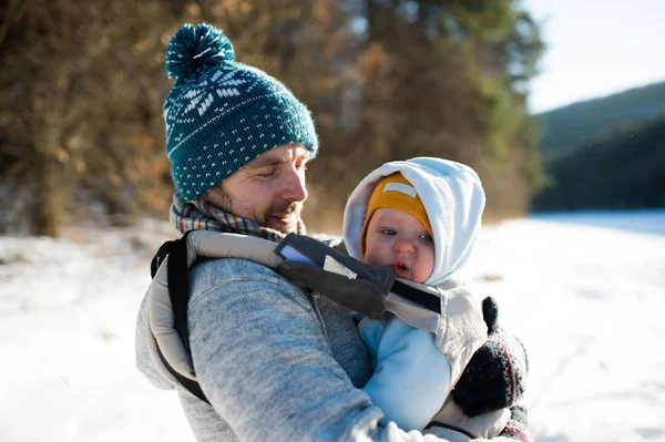 Батько тримає свого сина в дитячому носії. Сонячна зимова природа . — стокове фото