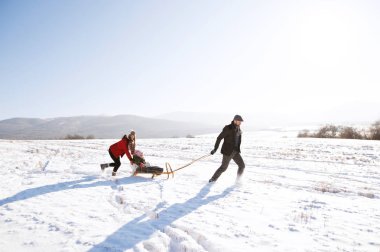Anne üzerinde kızak, babası onu çekerek iterek kızı. Kış na