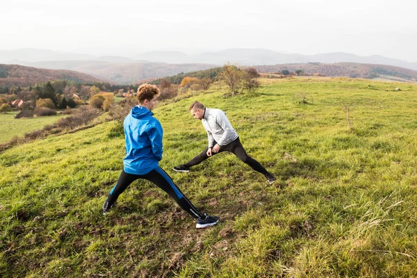 Dos jóvenes corredores hipster en la naturaleza soleada otoño estirando las piernas —  Fotos de Stock