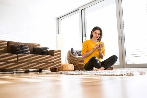 Kvinna hemma sitter på mattan, anläggning smart telefon, textning — Stockfoto