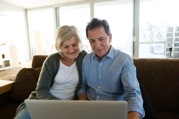 Senior couple with laptop sitting on a couch in living room — Stock Photo, Image