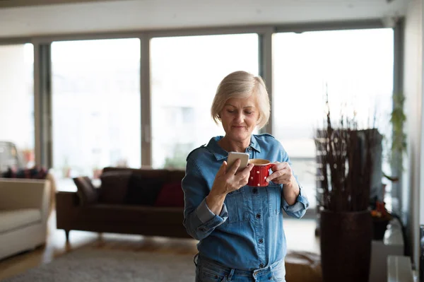 Mulher sênior com smartphone e café em casa — Fotografia de Stock