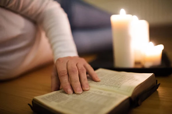 Oigenkännlig kvinna läser Bibeln. Brinnande ljus bredvid henne. — Stockfoto