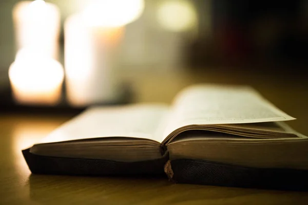 Біблія покладена на дерев'яну підлогу, палаючі свічки на задньому плані — стокове фото