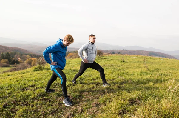 Two young hipster runners in sunny autumn nature stretching legs — Stock Photo, Image