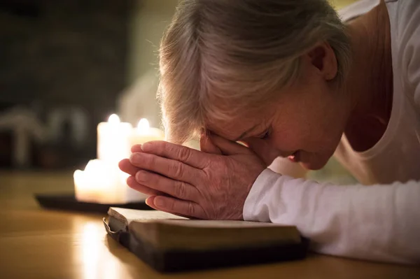 Senior Kvinna be, händerna knäppta tillsammans på hennes bibel. — Stockfoto