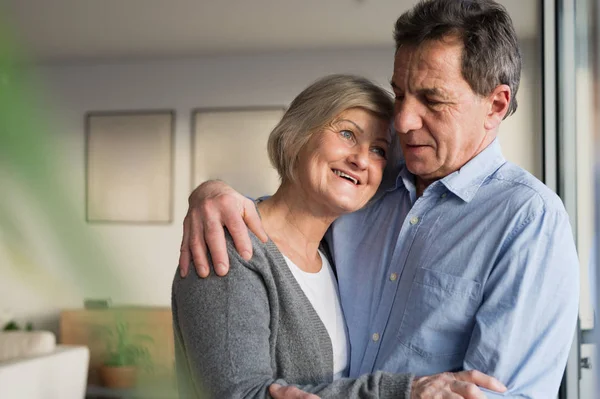 Senior couple in living room standing at the window, hugging — Stock Photo, Image