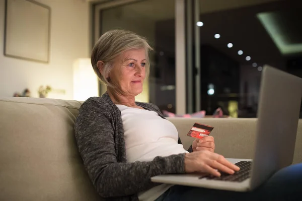 Старшая женщина с ноутбуком сидит на диване покупки онлайн — стоковое фото
