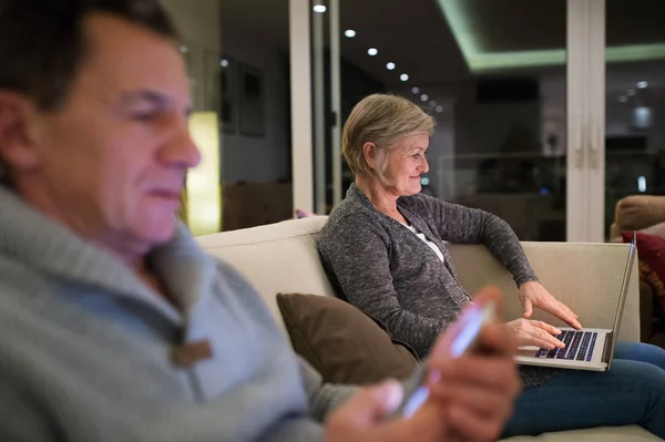 Senior couple with laptop and smartphone sitting on couch — Stock Photo, Image