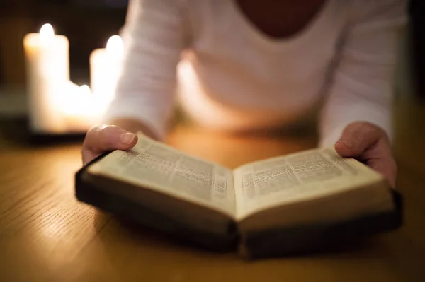 Oigenkännlig kvinna läser Bibeln. Brinnande ljus bredvid henne. — Stockfoto