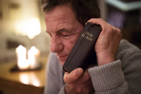 Старший молится, держа Библию в руках, глаза закрыты . — стоковое фото
