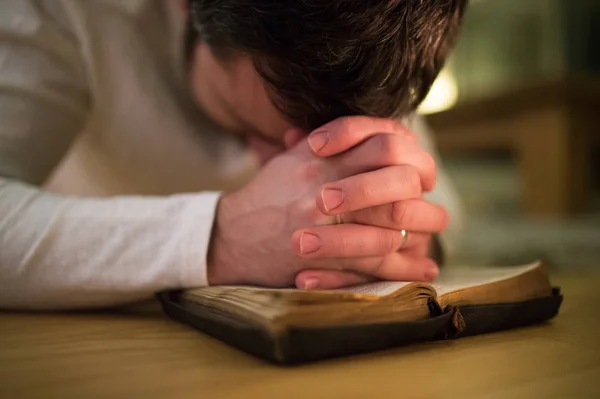 Невпізнаваний чоловік молиться, на колінах на підлозі, руки на Біблії — стокове фото