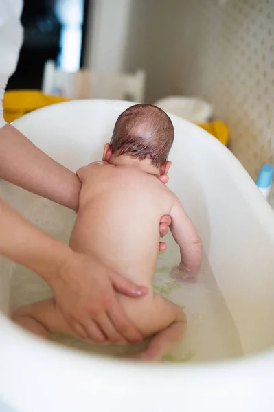 Oigenkännlig mor badar sin son i vit liten plast bat — Stockfoto
