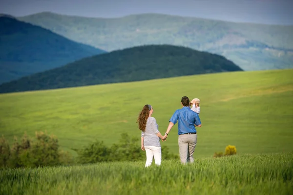 Young family on a walk against green fields and hills — Stock Photo, Image