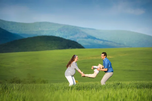 Young family on a walk against green fields and hills — Stock Photo, Image