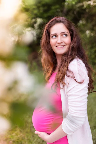 Schöne schwangere Frauen, die ihren Bauch halten. Sommerliche Natur. — Stockfoto