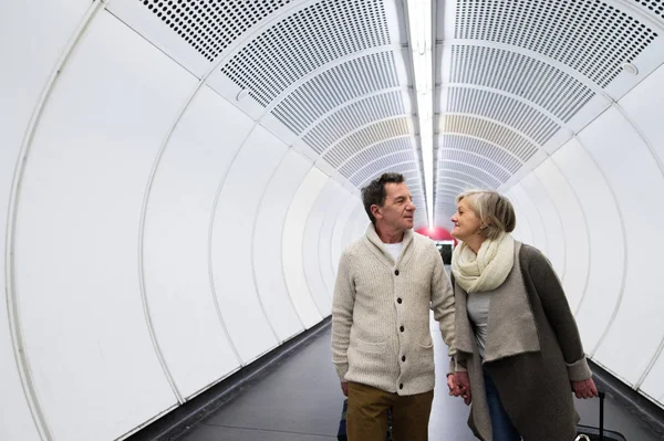 Casal sênior no corredor do metrô puxando bagagem de carrinho . — Fotografia de Stock