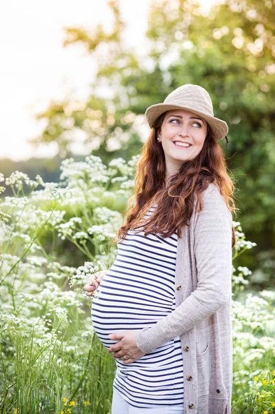Schöne schwangere Frauen, die ihren Bauch halten. Sommerliche Natur. — Stockfoto