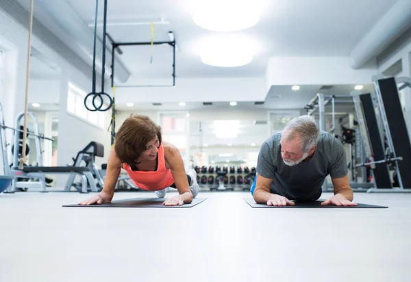Äldre par i gymmet i planka position arbetar abs — Stockfoto