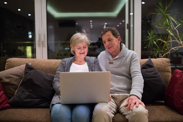 Senior couple with laptop sitting on a couch in living room — Stock Photo, Image